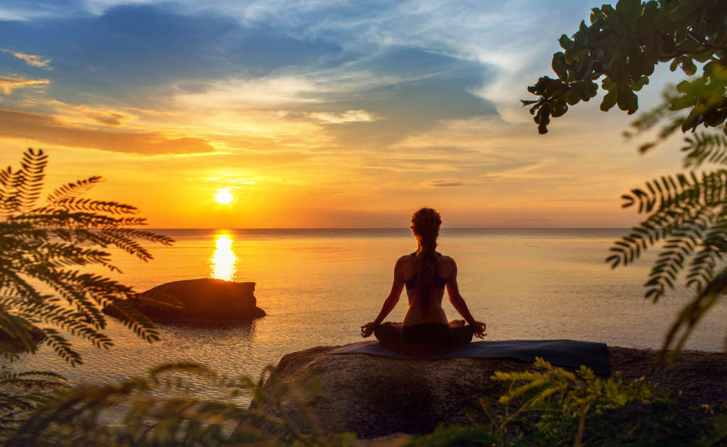 Kobieta siedząca w pozycji kwiatu lotosu na tle zachodzącego słońca - medytacja devavani